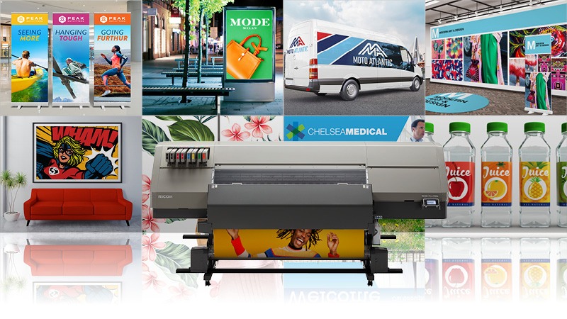 Page: Sheet-fed This is a Large Ricoh Commercial/Industrial Sheet-fed Production printer centered. It is a large and wide medium gray rectangular shaped device with dark gray accents and a large smart touch screen operation panel positioned at the top-right of the machine. Photo is on a backdrop adorned with oversized, high quality, richly colored poster advertisements for a variety of products and events.